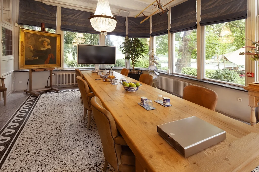 Foto van de zakelijke ruimte van Logement aan de Vecht. Er is een lange tafel zichtbaar met hapjes en een beamer op tafel. Aan de kop van de tafel staat een tv scherm voor presentaties.
